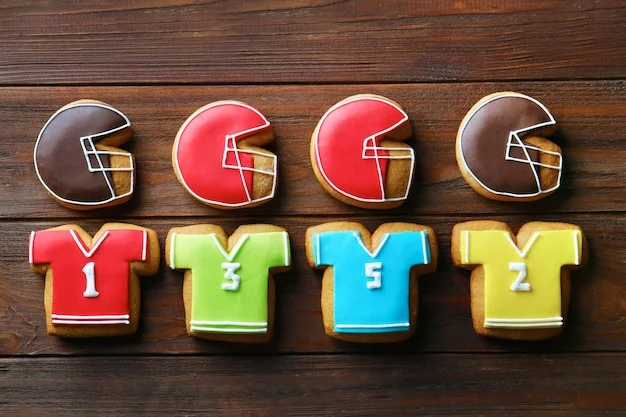 A flat lay of eight American football-themed cookies on a wooden table, featuring helmets (brown, red) and jerseys (red, green, blue, yellow) with numbers.