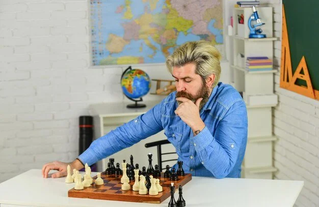 Bearded man in blue shirt intensely focused on a chess game, hand on chin, with a world map and globe in the background.