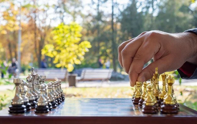 A hand moves a golden chess pawn on a wooden board, set against a blurred background of autumn trees in a park.